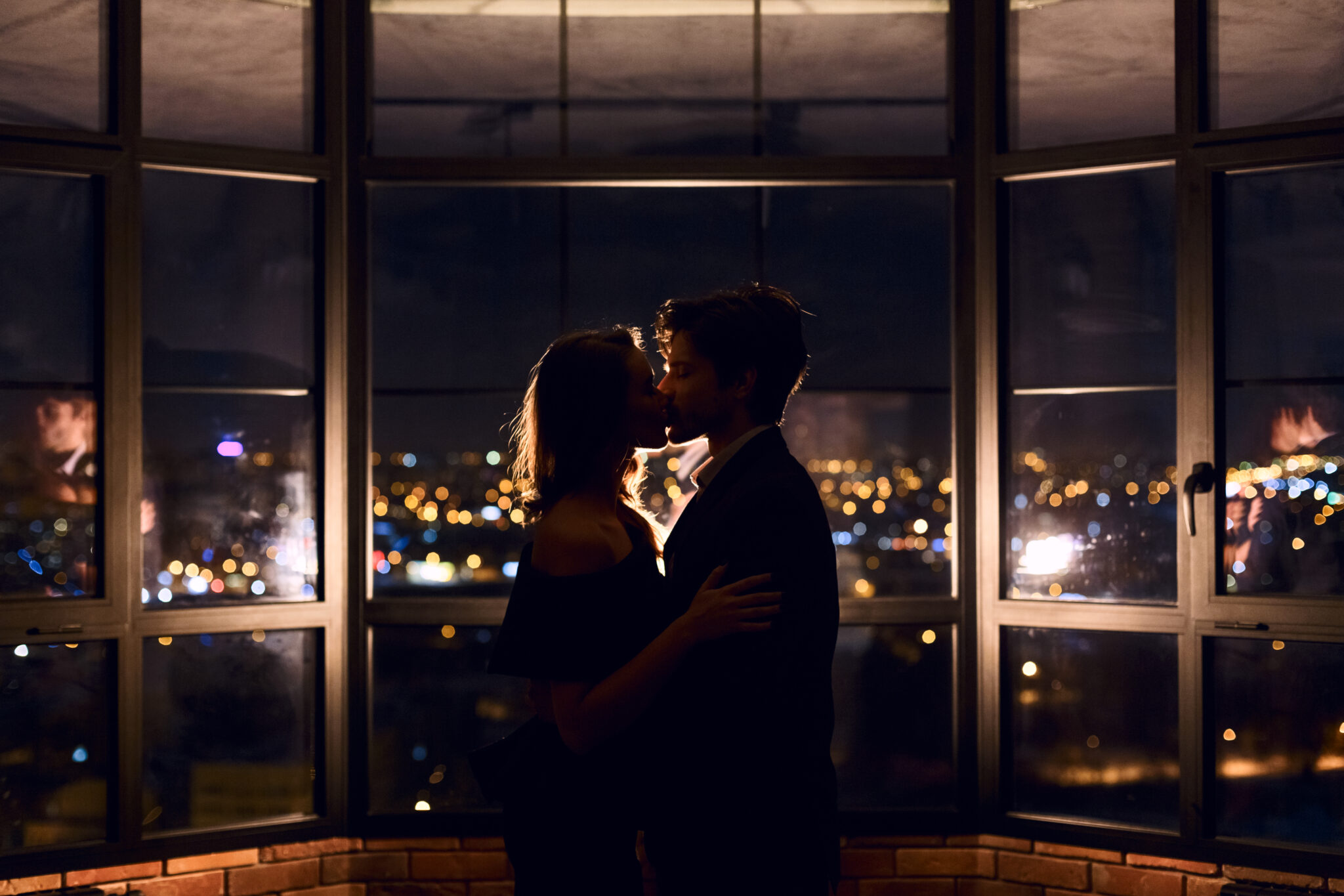 un cuplu format dintr-un barbat si o femeie se saruta noaptea langa geam